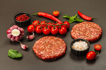 Raw steak cutlets from minced beef meat on black stone background. Fresh vegetables, mint