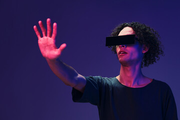 Excited stylish tanned curly man in black t-shirt eyewear touches invisible object posing isolated...