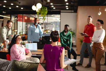 Happy creative multiracial businesswomen and businessmen discussing in office