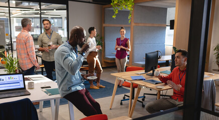 Multiracial colleagues discussing while having coffee during break in office