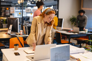 Caucasian young businesswoman working on laptop at desk in creative office