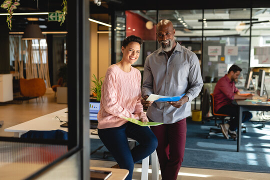 Portrait of smiling multiracial male and female colleagues with file in creative office