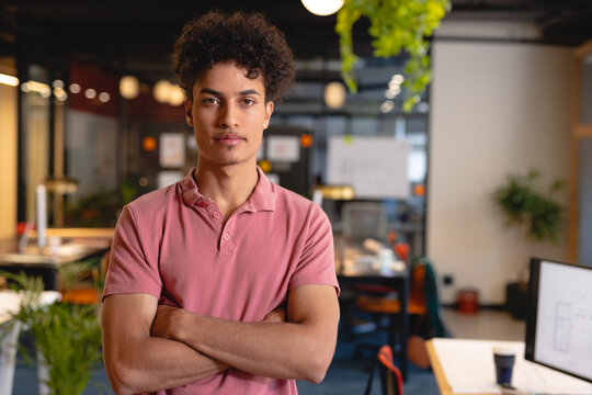 Portrait of confident biracial young businessman standing with arms crossed in creative office
