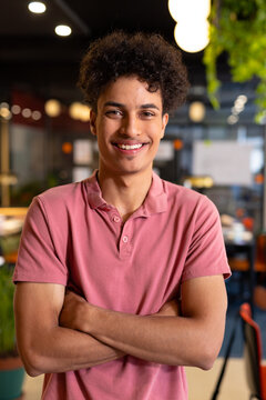 Portrait of smiling biracial young businessman standing with arms crossed in creative office