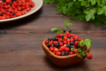 ripe wild berries, strawberries and blueberries in a wooden bowl on the table