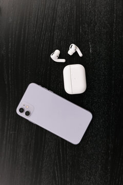 On The Black Table There Is A Purple Phone And Wireless White Vacuum Headphones With A Case.  