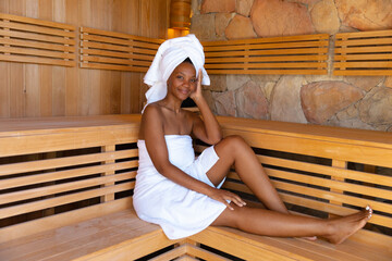 Portrait of young african american woman wrapped in towels sitting in sauna, copy space
