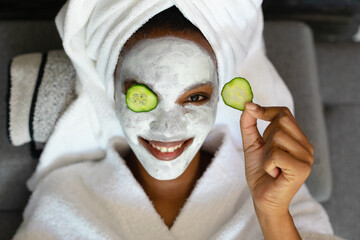 Portrait of smiling young african american woman with face cream, cucumber slices on face relaxing
