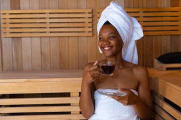 Cheerful young african american woman looking away while having healthy drink in sauna, copy space