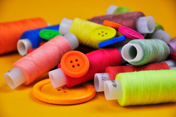 Set of multicolored buttons and Spools threads on a yellow background. Blurring.