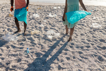 Low section of african american couple picking plastic waste on sand at beach - Powered by Adobe