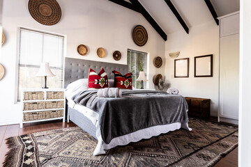 Bed with blankets and pillows and decorations hanging on white wall in modern bedroom, copy space