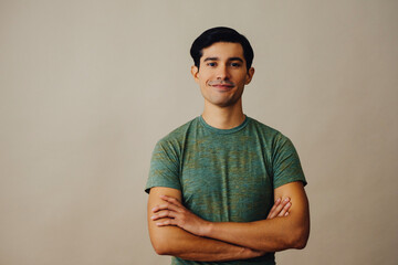 Portrait latino man with arms crossed and black hair smiling handsome young adult green t-shirt over gray background looking at camera studio shot