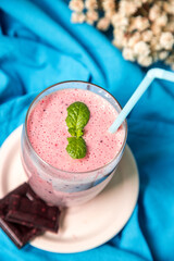 Fresh and delicious drink full of vitamins and antioxidants based on mixed red fruits in a tall glass with straw on a blue background. Red fruit smoothie with mint.