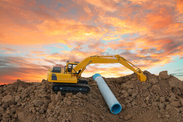 Excavator is digging in the construction site pipeline work ,on a sky background with bright orange...