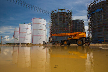 Obraz premium Constuction of an oil derrick crane, big oil tanks water background