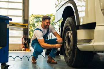 The mechanic squats next to the wheel of the truck and tightens the wheel screws. Use special...