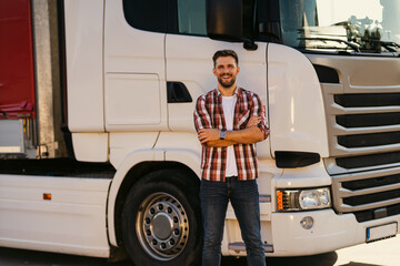 Portrait of young bearded man standing by his truck. Professional truck driver with crossed arms...