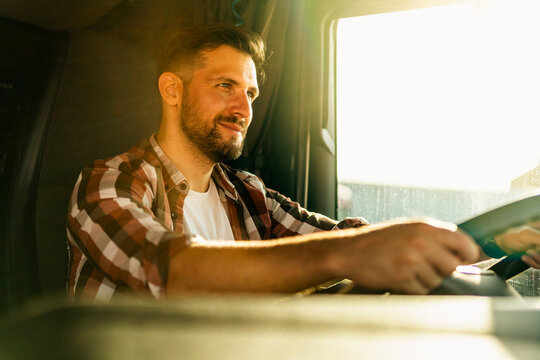 Professional Middle Aged Truck Driver In Casual Clothes Driving Truck Vehicle Going For A Long Transportation Route.