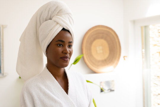 Young african american woman wearing head towel and bathrobe looking away in bathroom at home