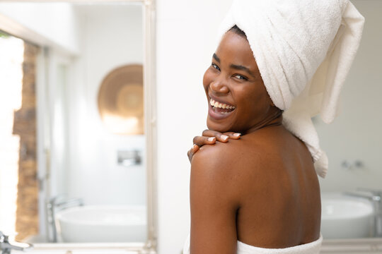 Portrait of young african american woman in towels laughing in bathroom at home, copy space