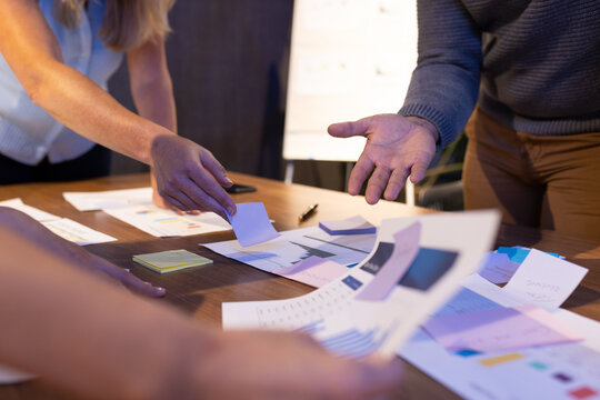 Midsection of multiracial colleagues gesturing while analyzing and discussing reports on table