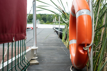 Orange lifebuoy hang on the pier, on the lake, on a summer day. Concept of a safe holiday.