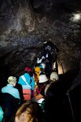 Tourists in the cave walk in a crowd along a narrow passage, an expedition of speleologists studies the karst abyss, the light of the lantern illuminates the walls of the cave.