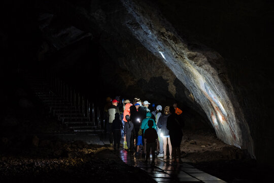 Excursion To The Cave A Group Of People Looking At The Wall Light From A Hand Lantern, An Organized Company Of People Exploring The Underground Beauties Of The Karst World.