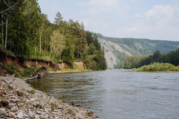 A calm river flows among the mountains, the nature of Russia is the Republic of Bashkortostan, a white river, a clay steep bank, a rock in the distance on the horizon.