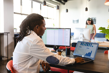 African american young businessman analyzing graphs in laptop at desk in creative office