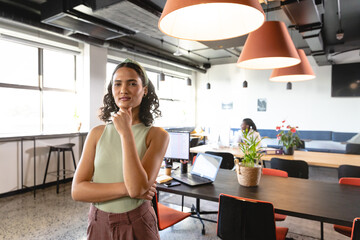 Portrait of confident young biracial businesswoman with hand on chin in creative office