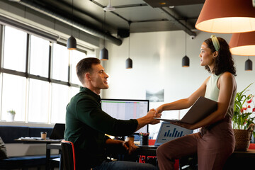 Multiracial young businessman and businesswoman handshaking in creative office