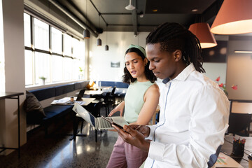 Multiracial young businessman and businesswoman with laptop and smart phone discussing in office