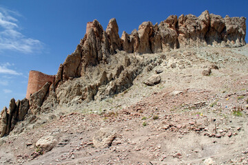 Fototapeta premium View of part of Dogubayazit Castle, which is located on a high cliff, with many sharp mountain peaks, against a background of bright blue sky with clouds, near the city of Dogubayazit, in the Eastern 