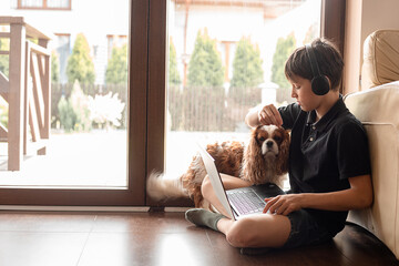 Side view of teenager boy sitting on floor with dog Cavalier King Charles spaniel at patio door, stroking, feeding pet.