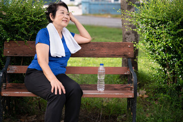 Asian senior woman tired and rest with towel and pure water in plastic bottle after walking or...