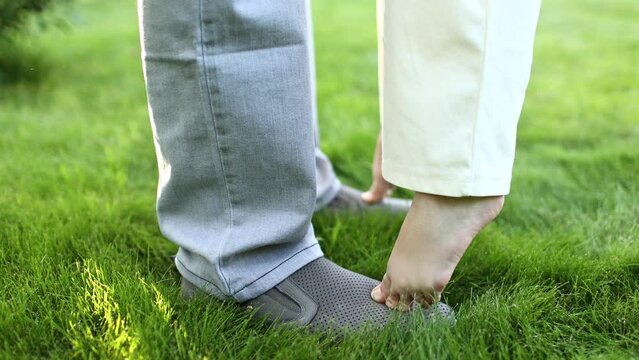 Child Fathers Feet Standing. The legs of the child girl stand on the feet of the father, dad supports the little daughter. Adorable feet at nature on a summer green meadow