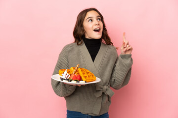 Little girl holding waffles isolated on pink background thinking an idea pointing the finger up