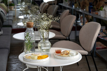 White plate with fried curd pancakes or syrniki, horizontal shot, sprinkled with coconut. In the background is the interior of the restaurant.
