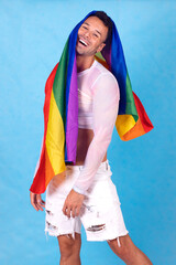 gay guy smiling with the pride flag over his head, blue background. . High quality photo