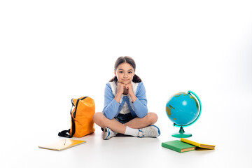 Preteen schoolchild looking at camera near backpack and globe on white background.
