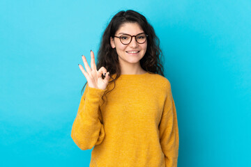 Teenager Russian girl isolated on blue background showing ok sign with fingers