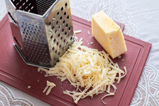 A pile of grated cheese on plastic board next to a grater