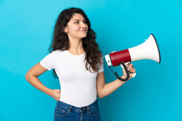 Teenager Russian girl isolated on blue background holding a megaphone and thinking