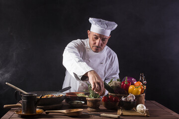 Male cook in white uniform and hat using aromatic herbs