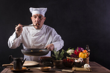 Male chef in white uniform is tasting food by using a wooden ladle at the kitchen of a restaurant