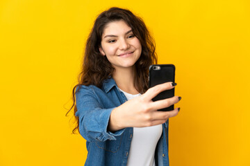 Fototapeta premium Teenager Russian girl isolated on yellow background making a selfie with mobile phone