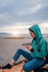 young woman sitting on the beach outdoors using or looking at cellphone portrait