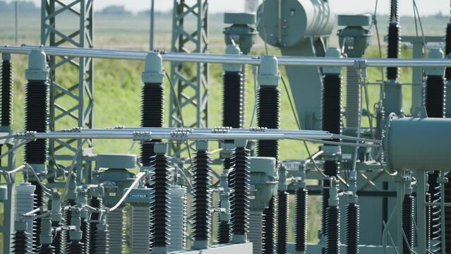 A close-up shot of an electrical power plant. Green fields in the background. Slow-motion, pan left.